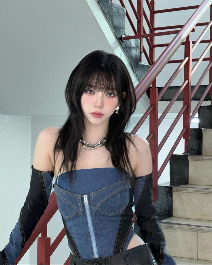 a woman with long black hair wearing a denim dress and gloves standing in front of stairs