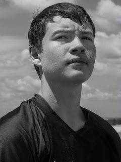 a young man standing on top of a beach next to the ocean under a cloudy sky