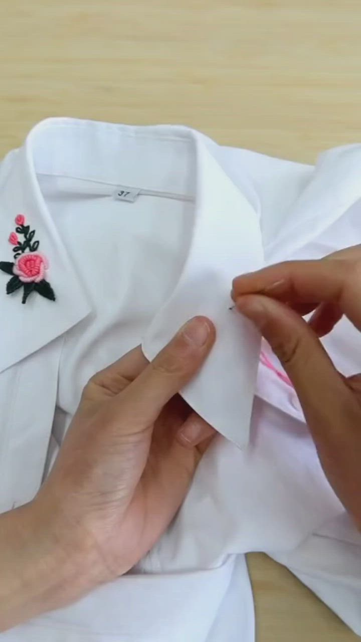 This may contain: a person is sewing a white shirt with pink flowers on the lapel and collar