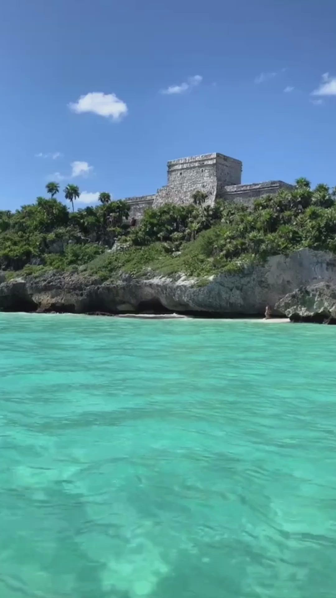 This may contain: an island in the middle of clear blue water with a castle on it's side