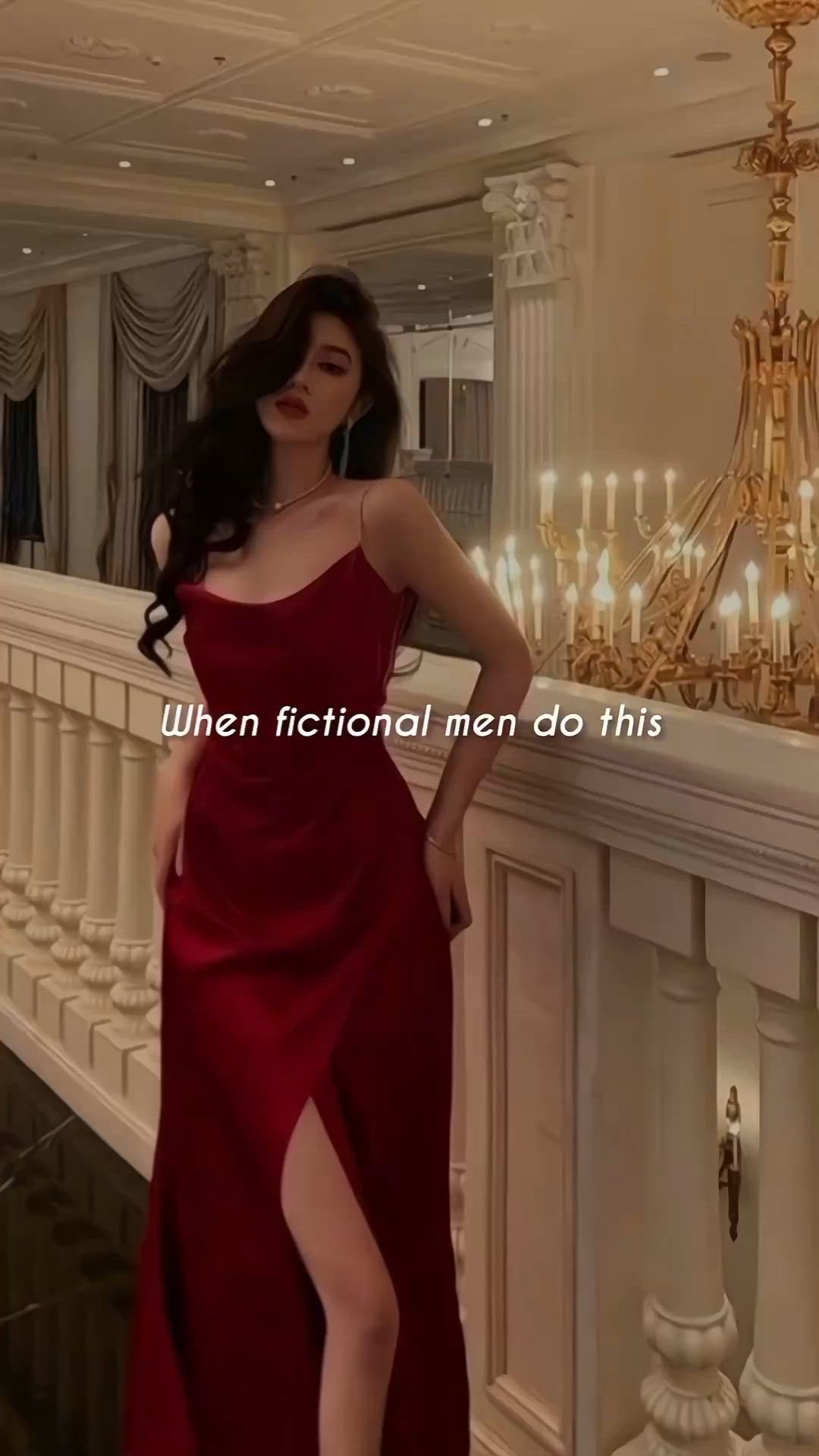 This may contain: a woman in a red dress standing next to a wall with chandeliers on it