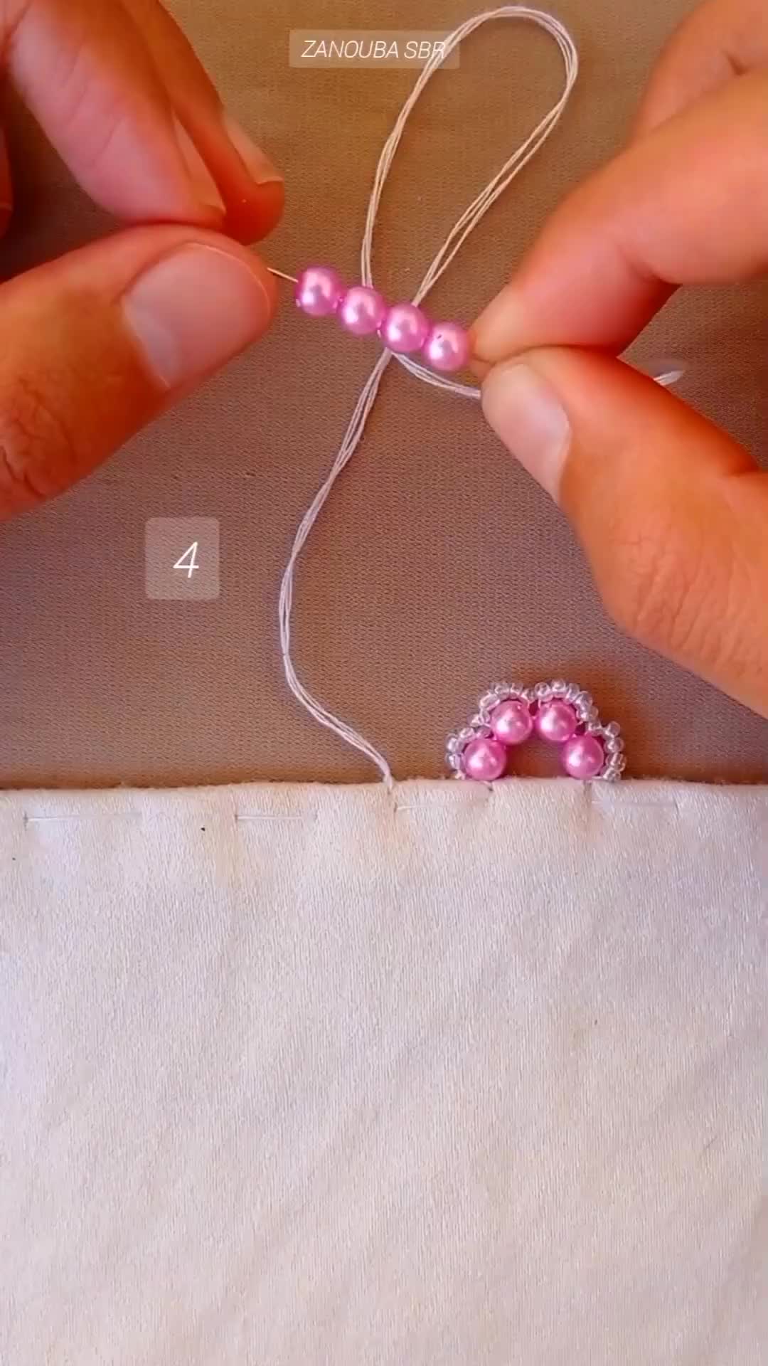 This may contain: two hands are working on some pink beaded beads with white thread, and one hand is holding the string