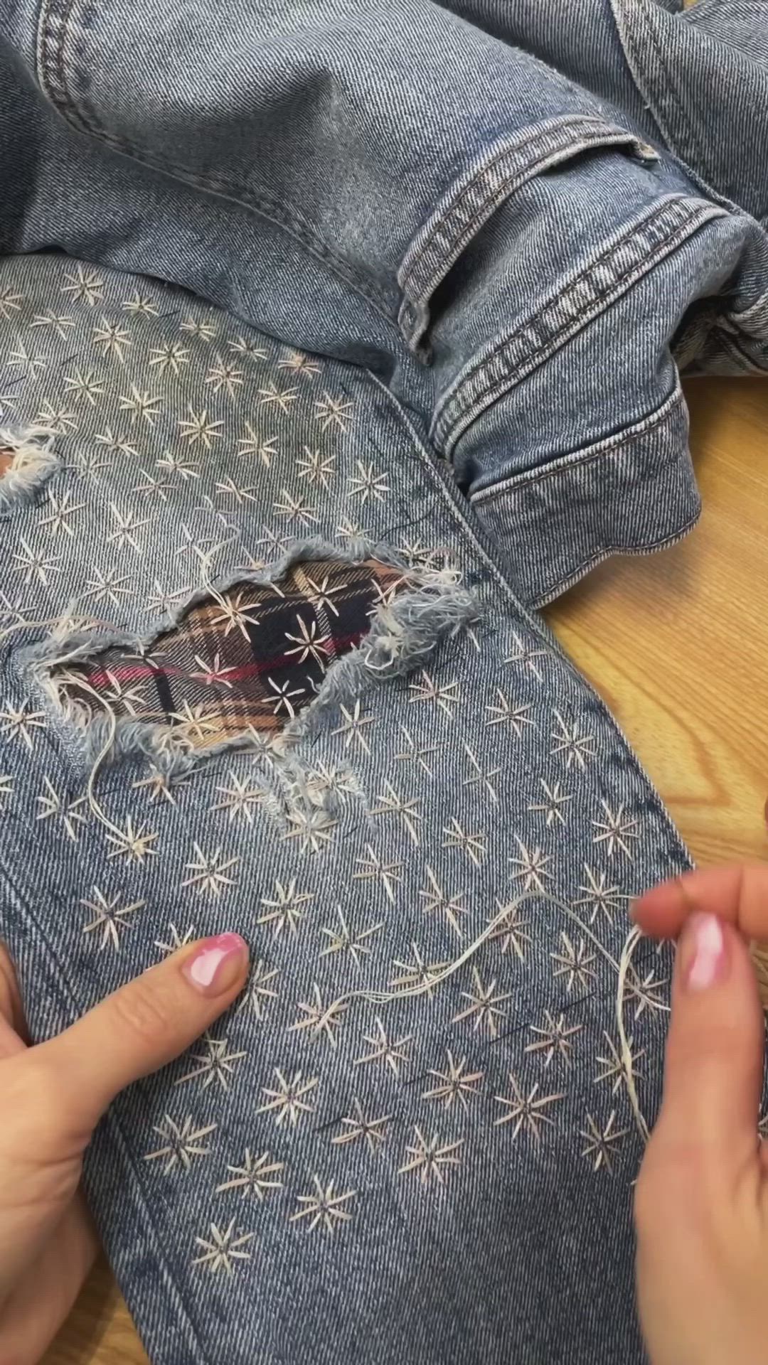 This may contain: two hands are working on an old pair of jeans that have been torn and stitched together