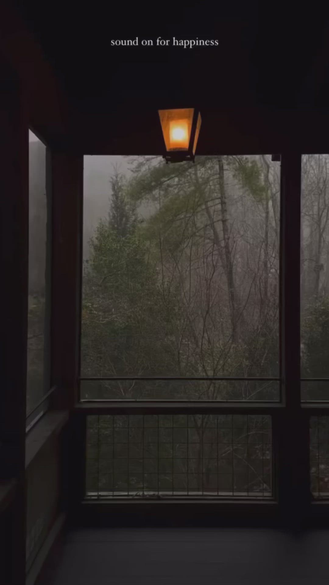 This may contain: an open window with a light on it in front of trees and foggy sky