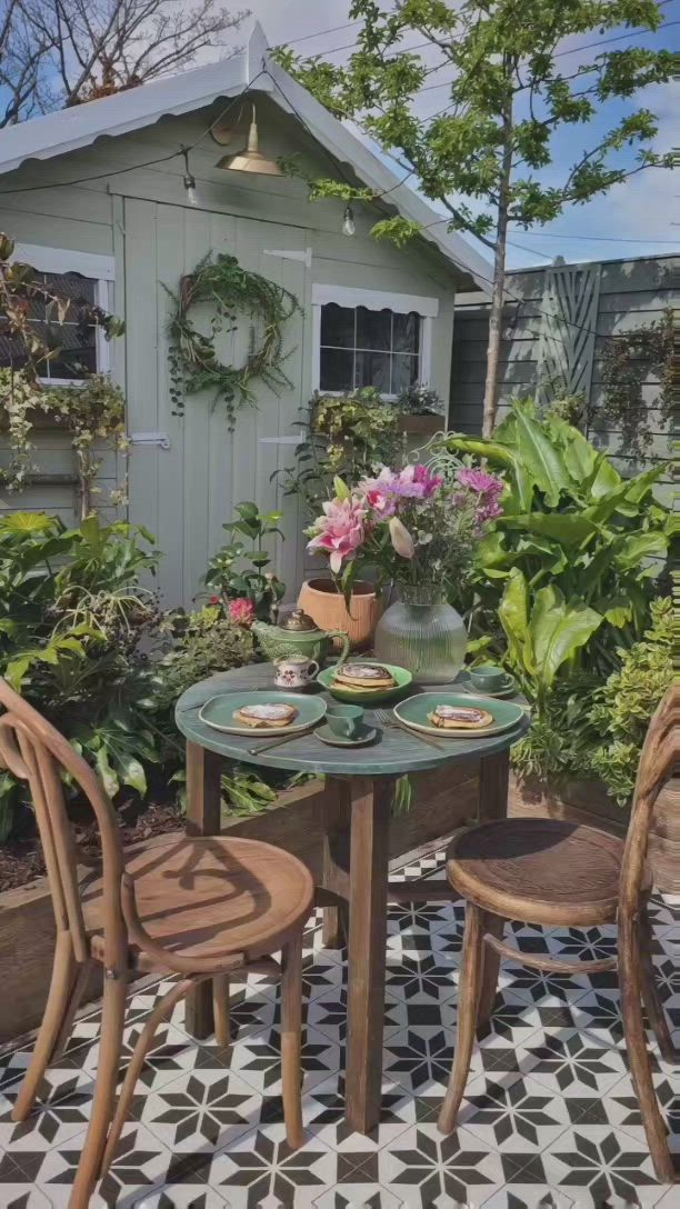 This may contain: two chairs and a table in front of a house with potted plants on it