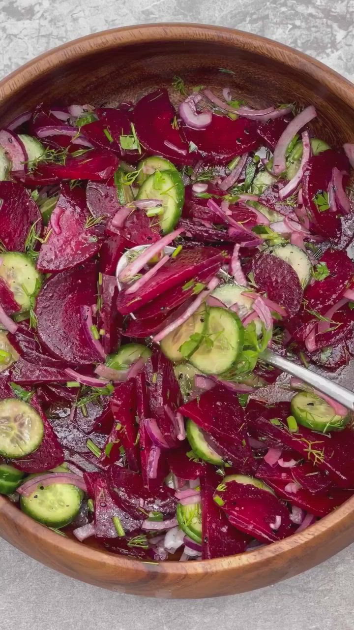 This may contain: a wooden bowl filled with sliced beets and cucumbers on top of a table