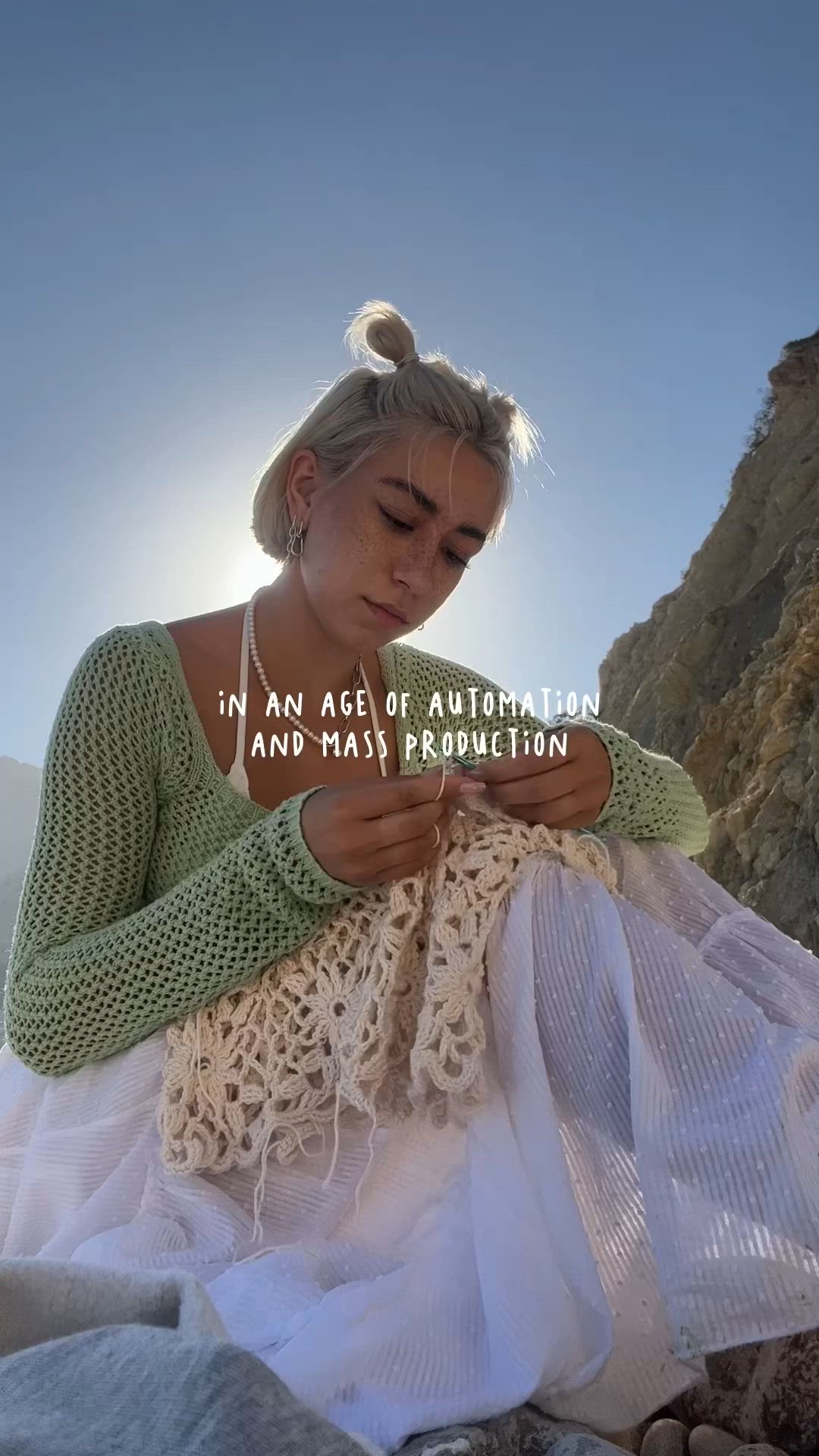 This may contain: a woman sitting on top of a rock next to a white netted dress and text that reads, in an age of auctionion and mass production