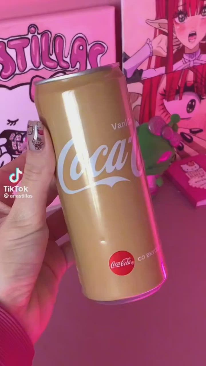 This may contain: a person holding up a can of coca cola in front of some pink wallpaper