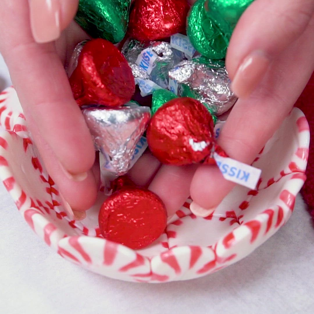 This may contain: a bowl filled with assorted candy on top of a white table next to red and green candies