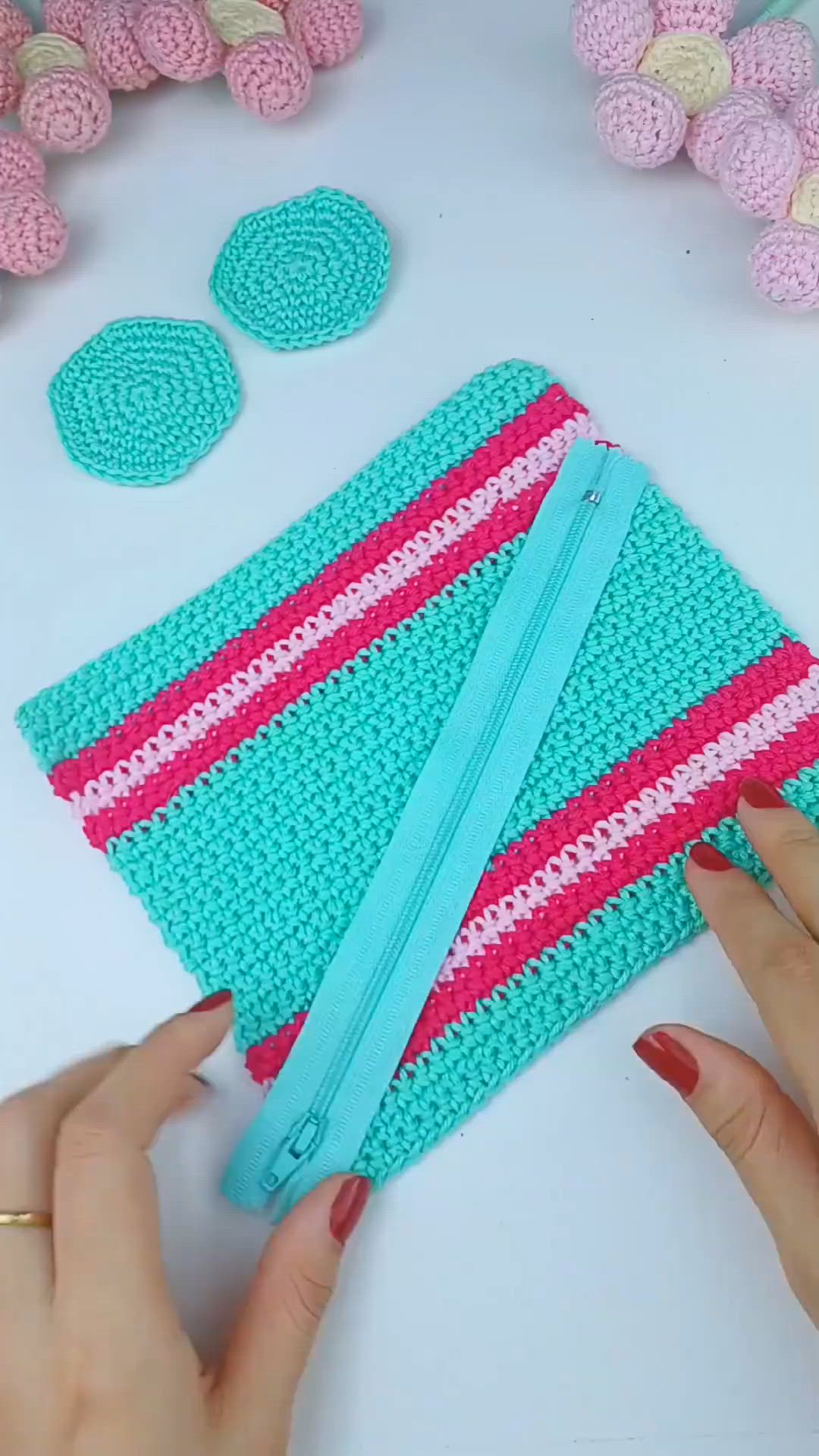 This may contain: a woman is making a crocheted purse with pink and blue strips on it