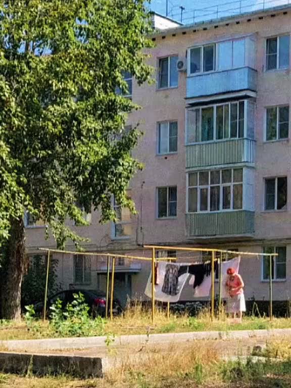 This may contain: two people standing in front of an apartment building with laundry hanging out to dry on the clothesline