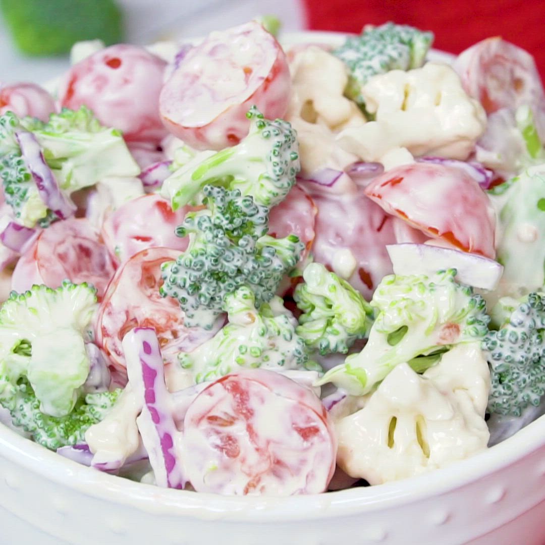 This may contain: broccoli and cauliflower salad in a white bowl on a red table