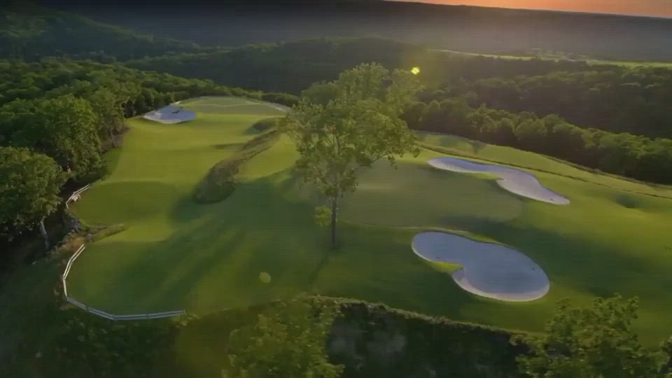 This may contain: an aerial view of a golf course with the sun setting in the distance and trees surrounding it