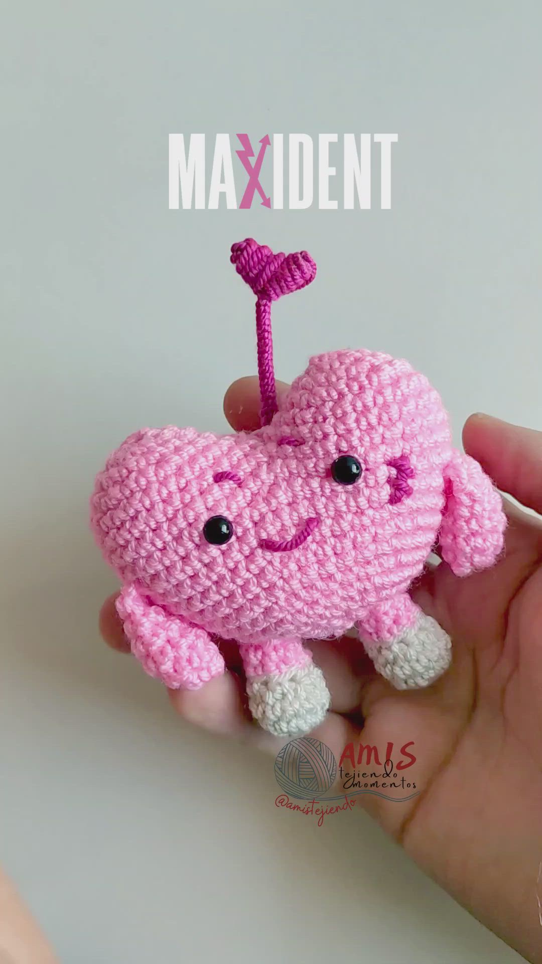 This may contain: a pink crocheted heart shaped object being held up by someone's hand