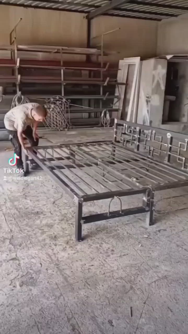 This may contain: a man is bending over to check out the metal bed frame in an industrial building