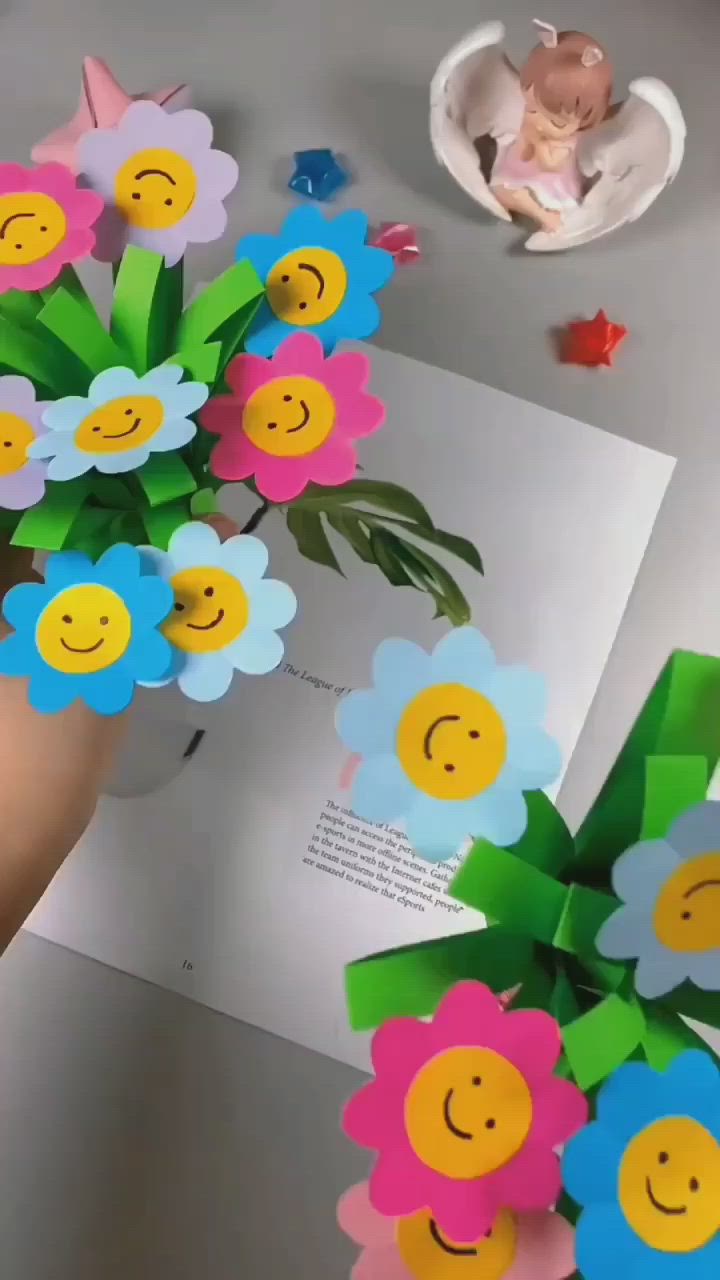 This may contain: a hand holding up some paper flowers with smiley faces on them