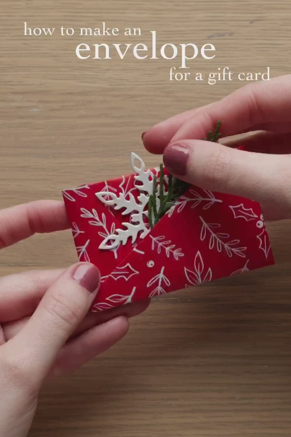 This may contain: two hands are holding an origami piece with snowflakes on it and the words how to make an envelope for a gift card