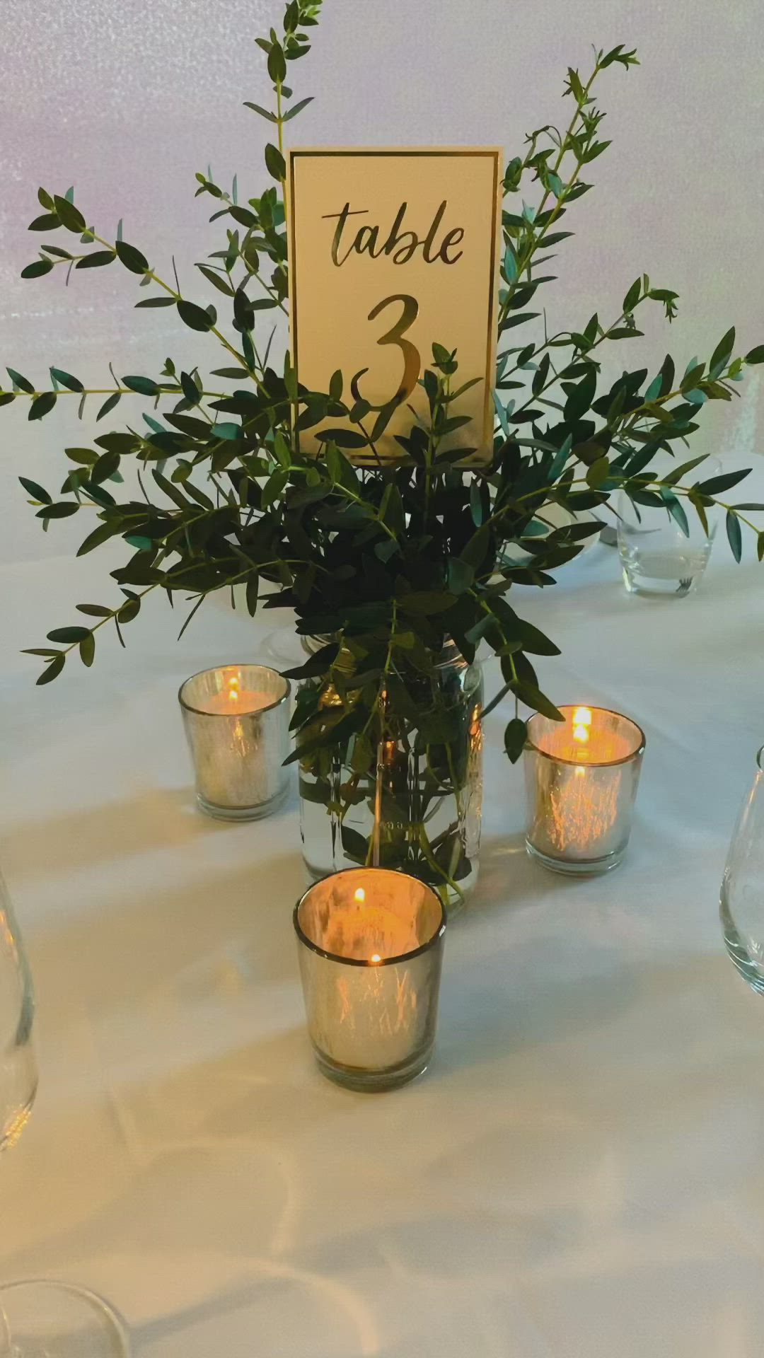 This may contain: the table is set with candles and greenery in glass vases, which are labeled table 2