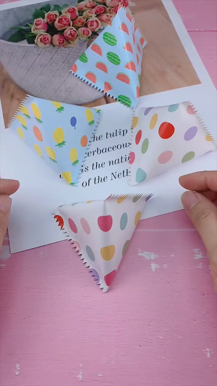 This may contain: two hands are holding up some paper with polka dots on it and one hand is holding a piece of paper that has been folded in the shape of a triangle