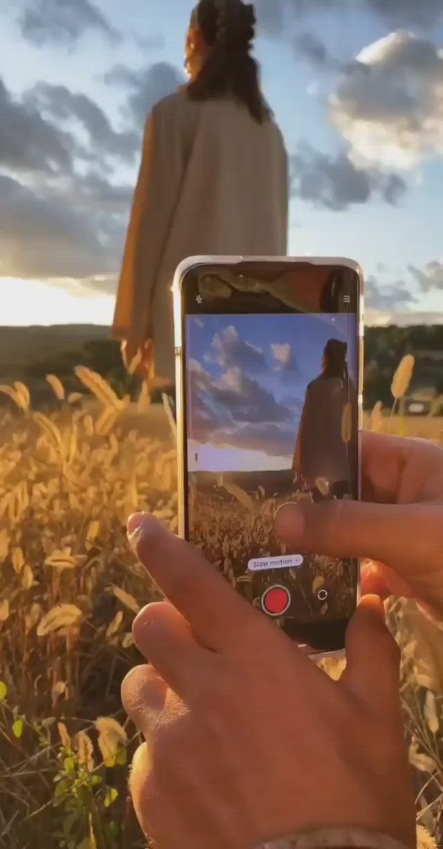 This may contain: a person taking a photo with their cell phone in a field at sunset or sunrise