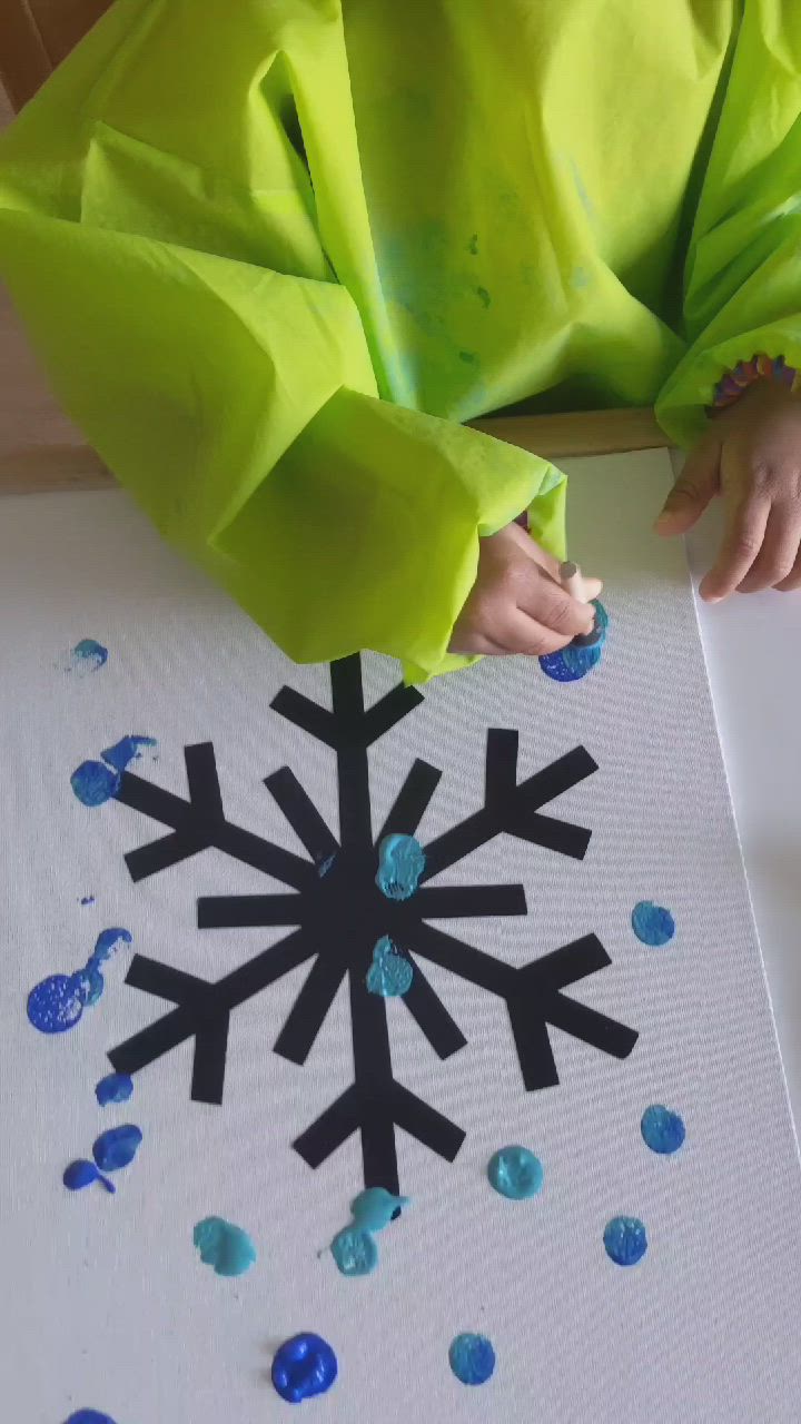 This may contain: a child is making a snowflake painting with blue and green dots on the paper