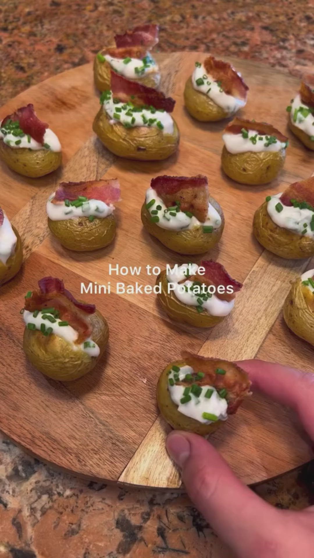 This may contain: mini baked potatoes with bacon and cream cheese on a wooden board being held by a person