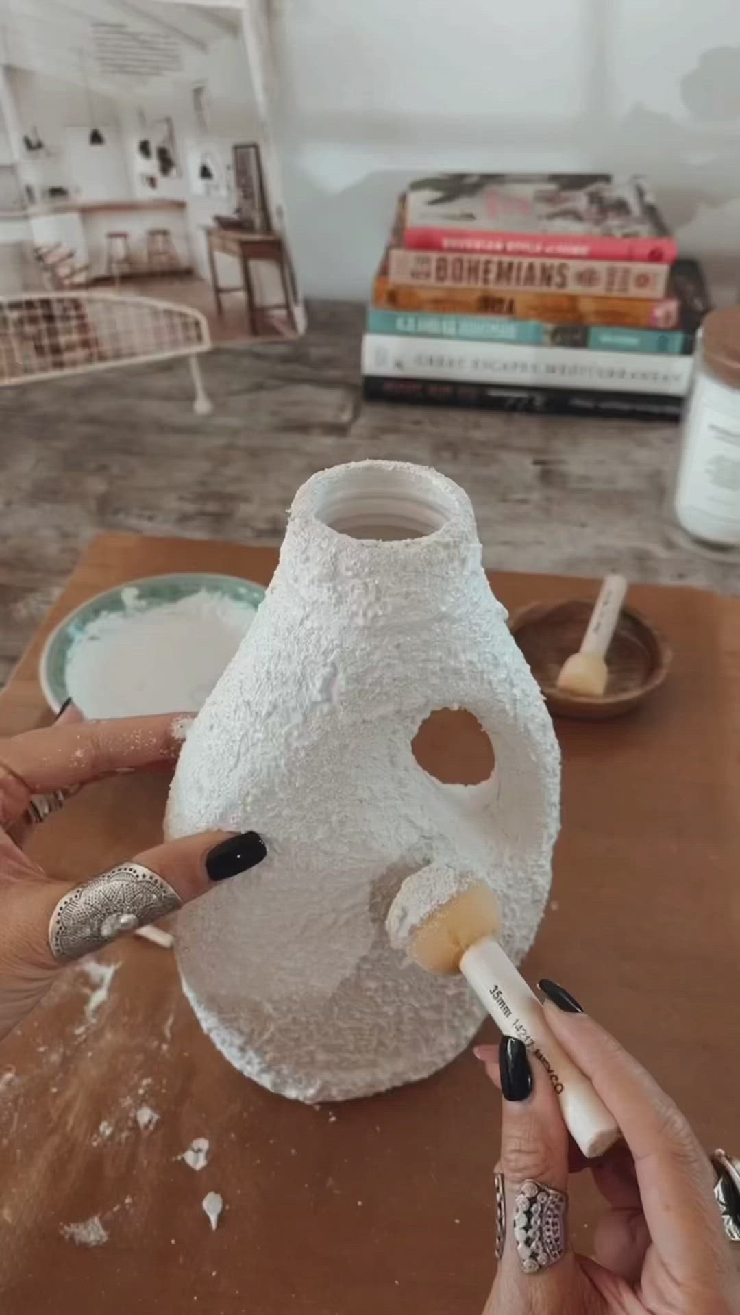 This may contain: two hands are painting a white vase on a table
