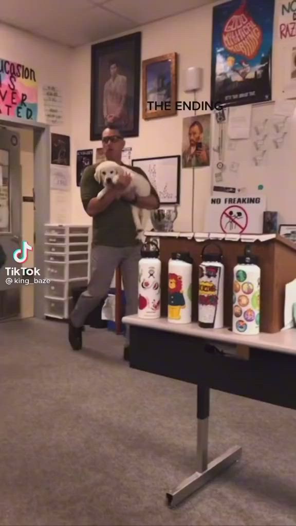 This may contain: a man holding a white dog in an office with lots of posters on the wall