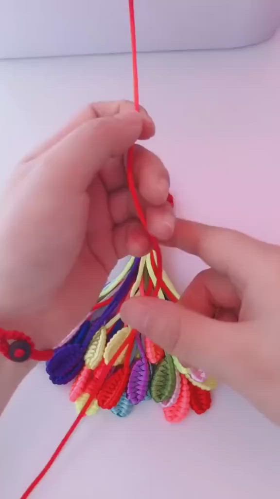 This may contain: someone is knitting something with red thread on a white surface and another person is holding the string in their hand