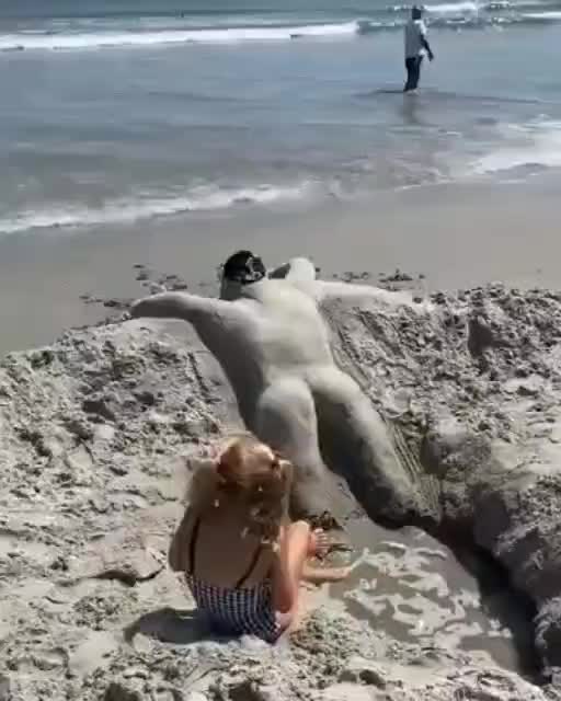 This may contain: a woman laying on the beach next to a dog and another person standing in the water