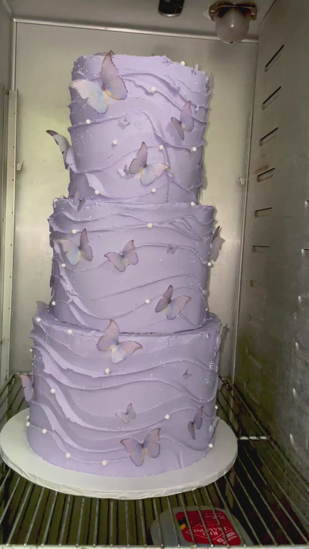 This may contain: a large purple cake sitting inside of a refrigerator filled with lots of white frosting