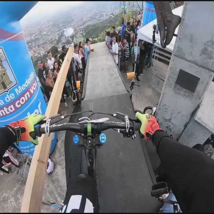 This may contain: a man riding a bike down a ramp next to a group of people on top of a building