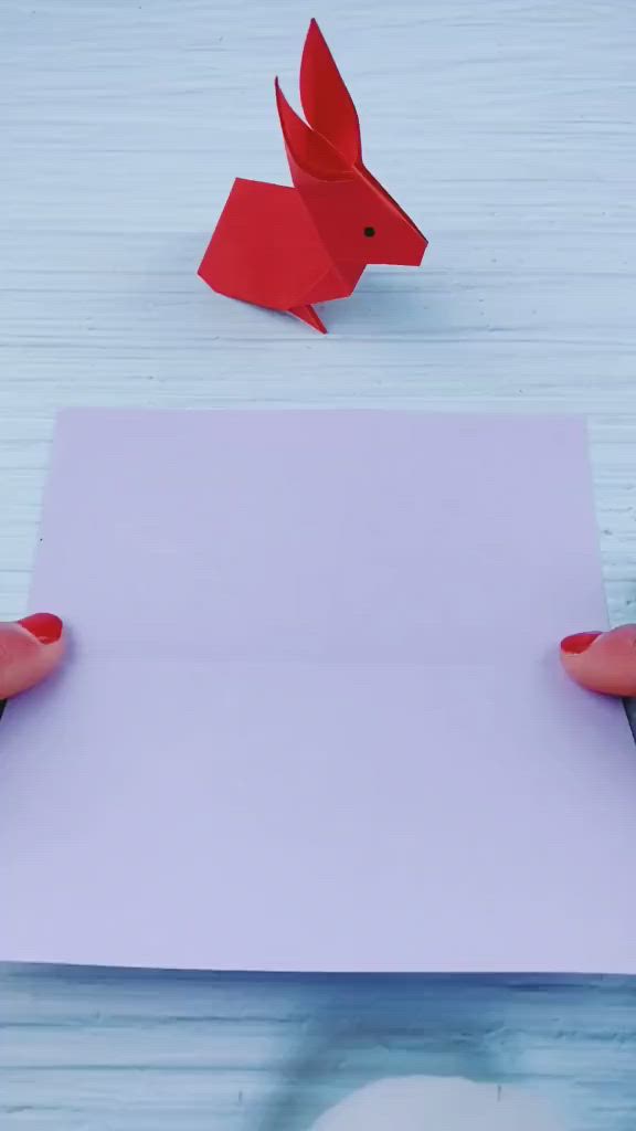 This may contain: two hands holding an empty piece of paper with a red origami bird on it