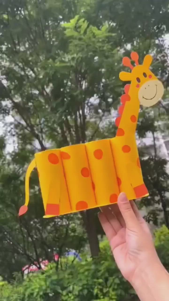 This may contain: a hand holding an origami giraffe with trees in the background