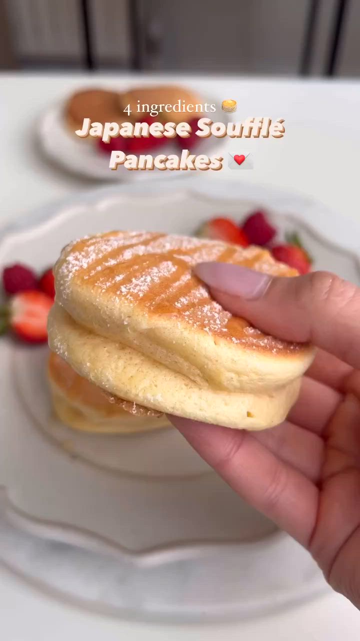 This may contain: a person is holding some pancakes on a plate with strawberries and syrup in the background