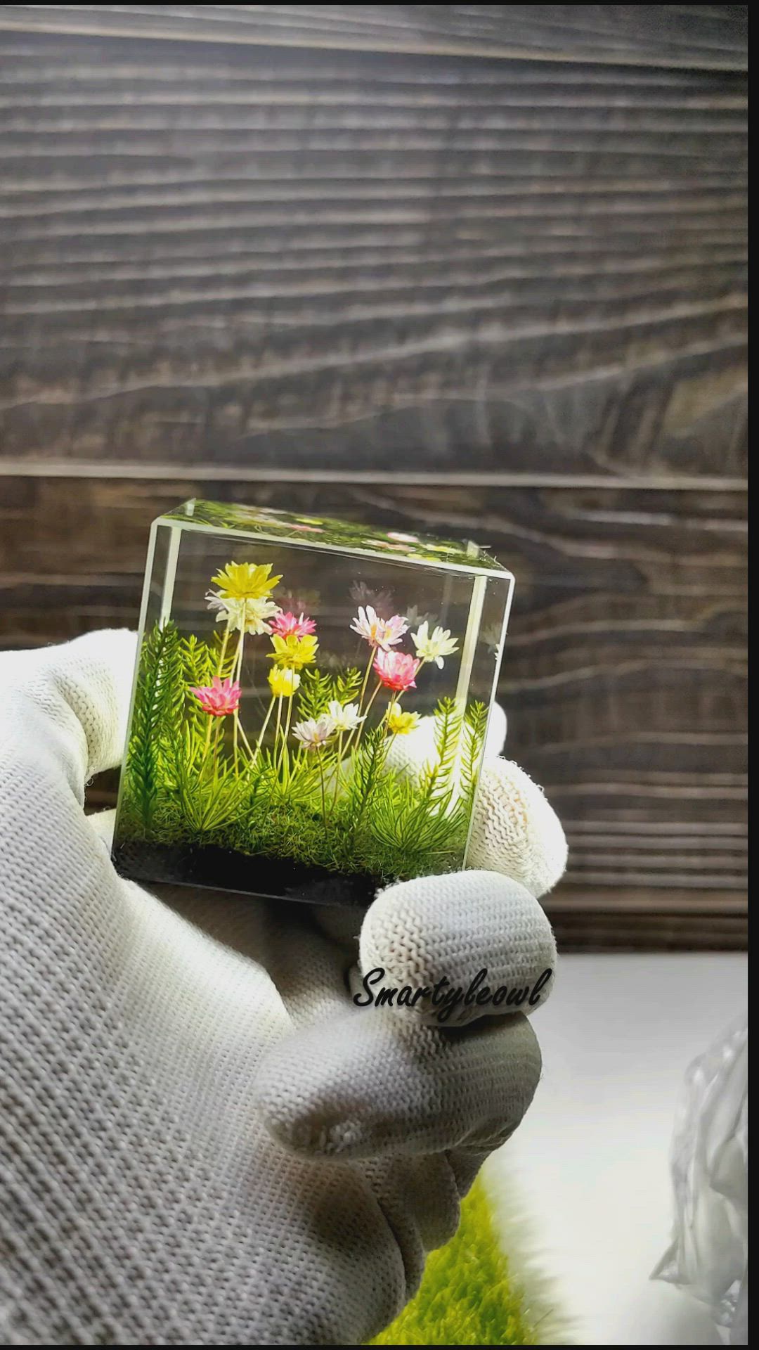 This may contain: a hand holding a small box with flowers on it and the words flower resinn diorama