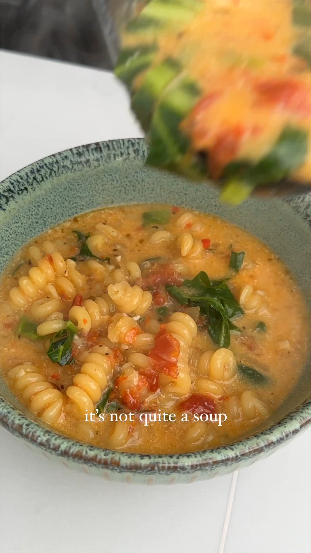 This may contain: a bowl filled with pasta and spinach soup on top of a table next to a pine cone