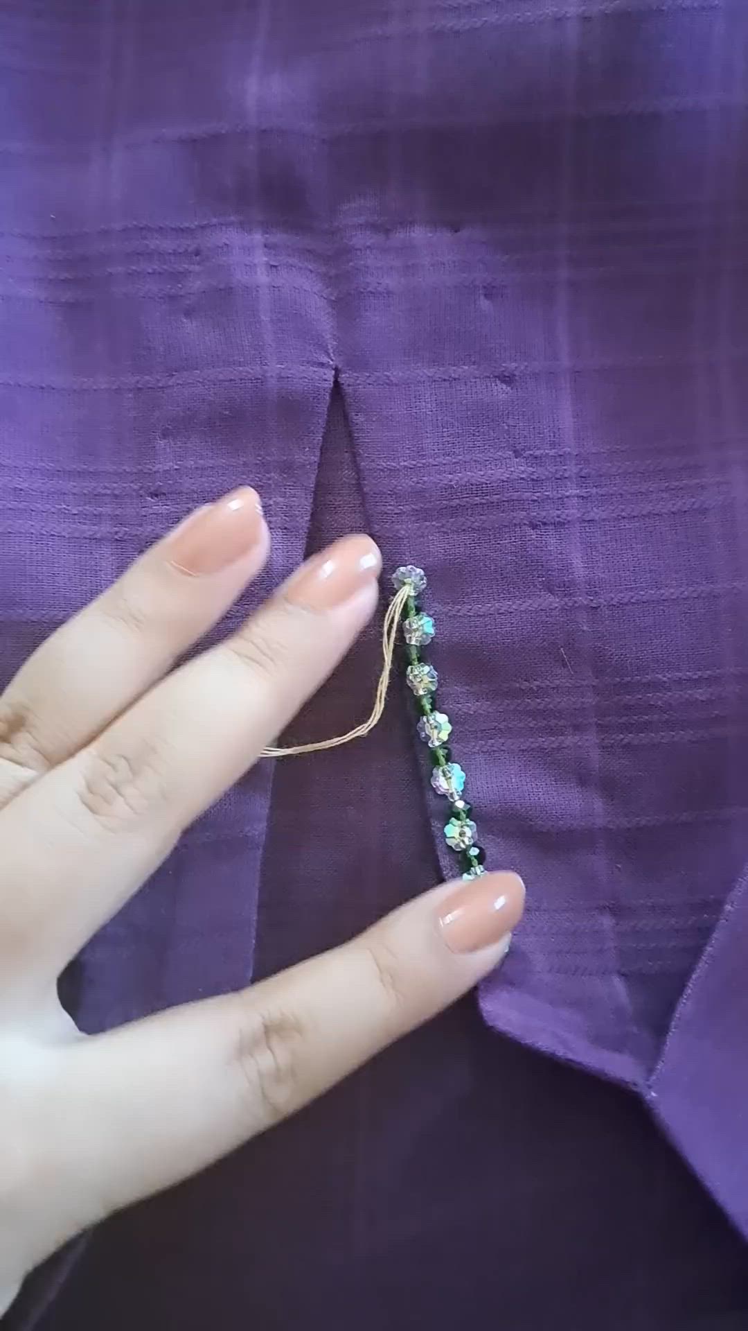 This may contain: a woman's hand is holding a beaded string on her purple shirt,