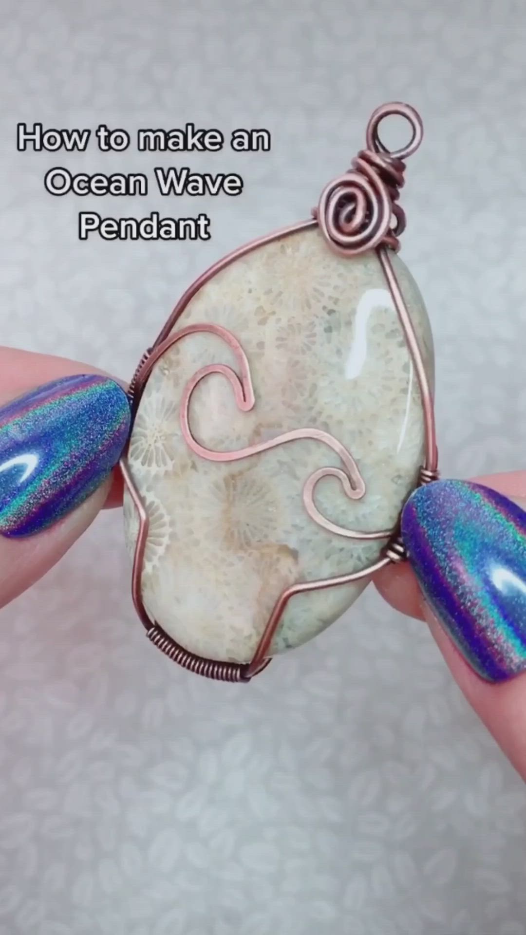 This may contain: a person holding a wire wrapped pendant with blue and white designs on it's face