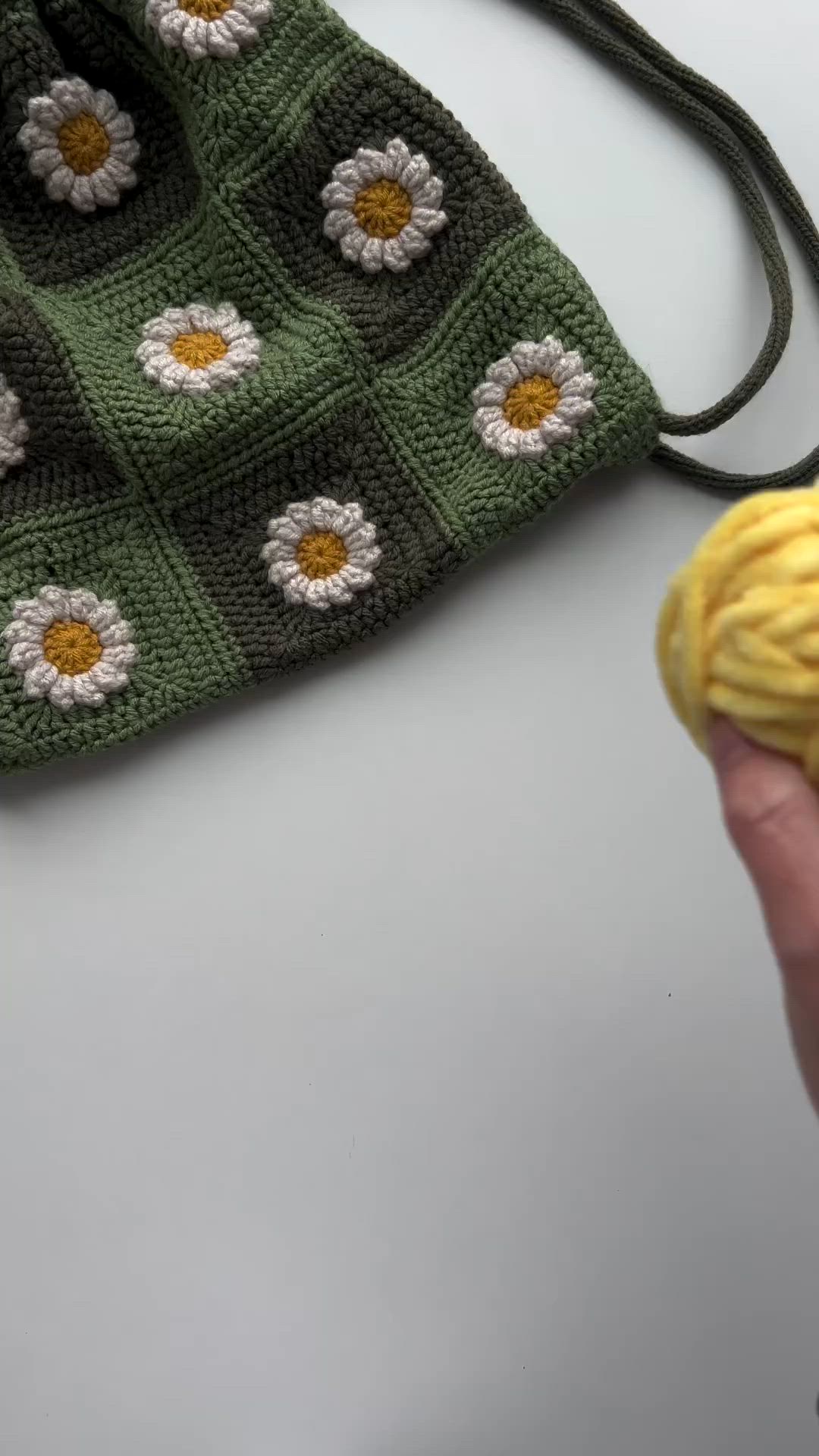 This may contain: a hand is holding a yellow object in front of a crocheted bag