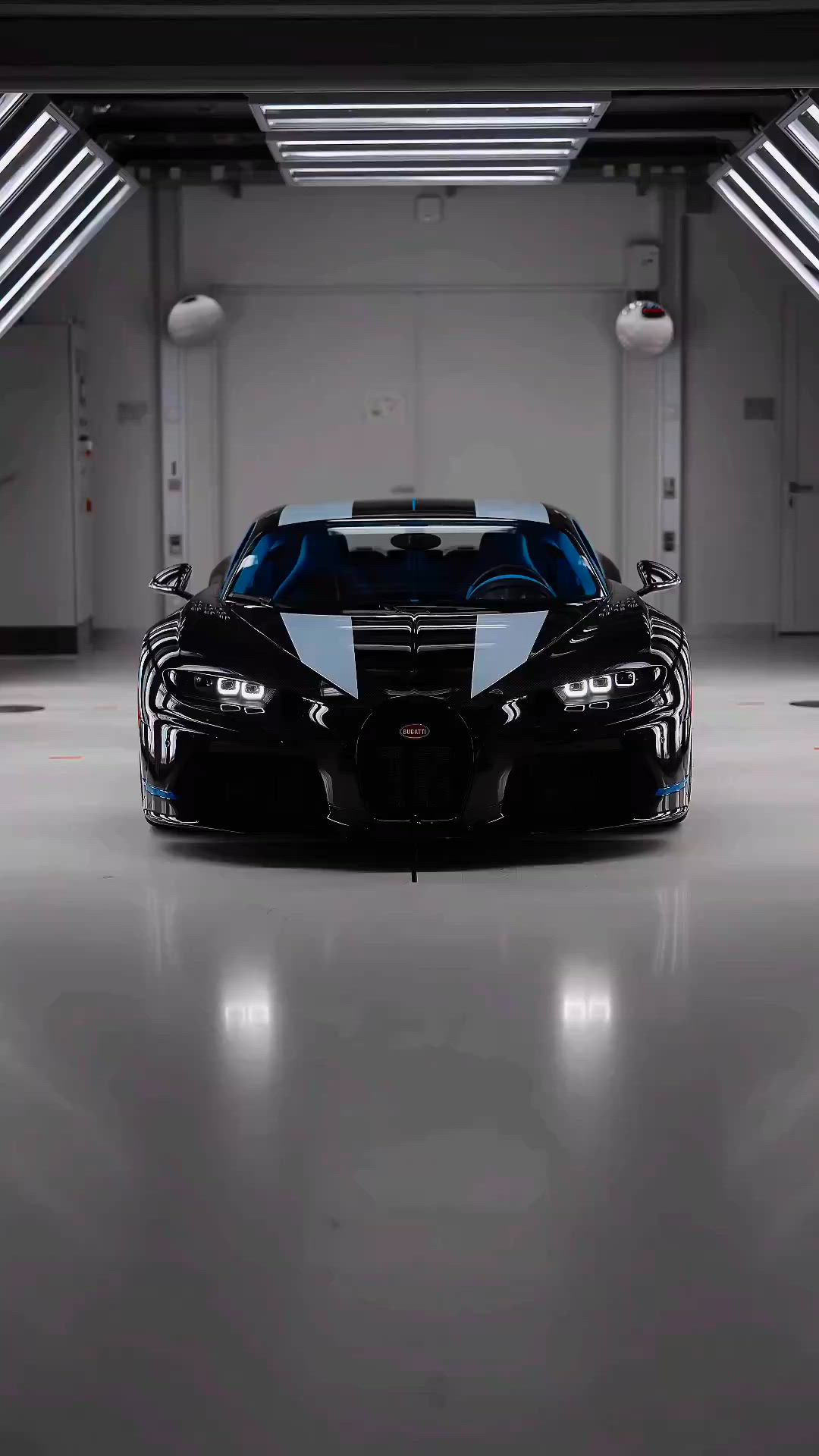 This may contain: a black and blue bugatti car in a garage with lights on the ceiling