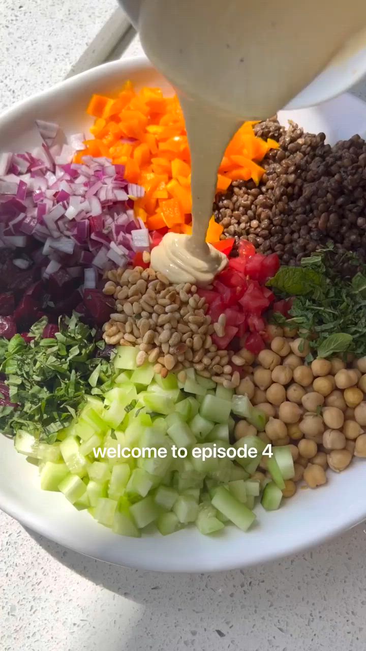 This may contain: a bowl filled with vegetables and dressing being drizzled on top of it