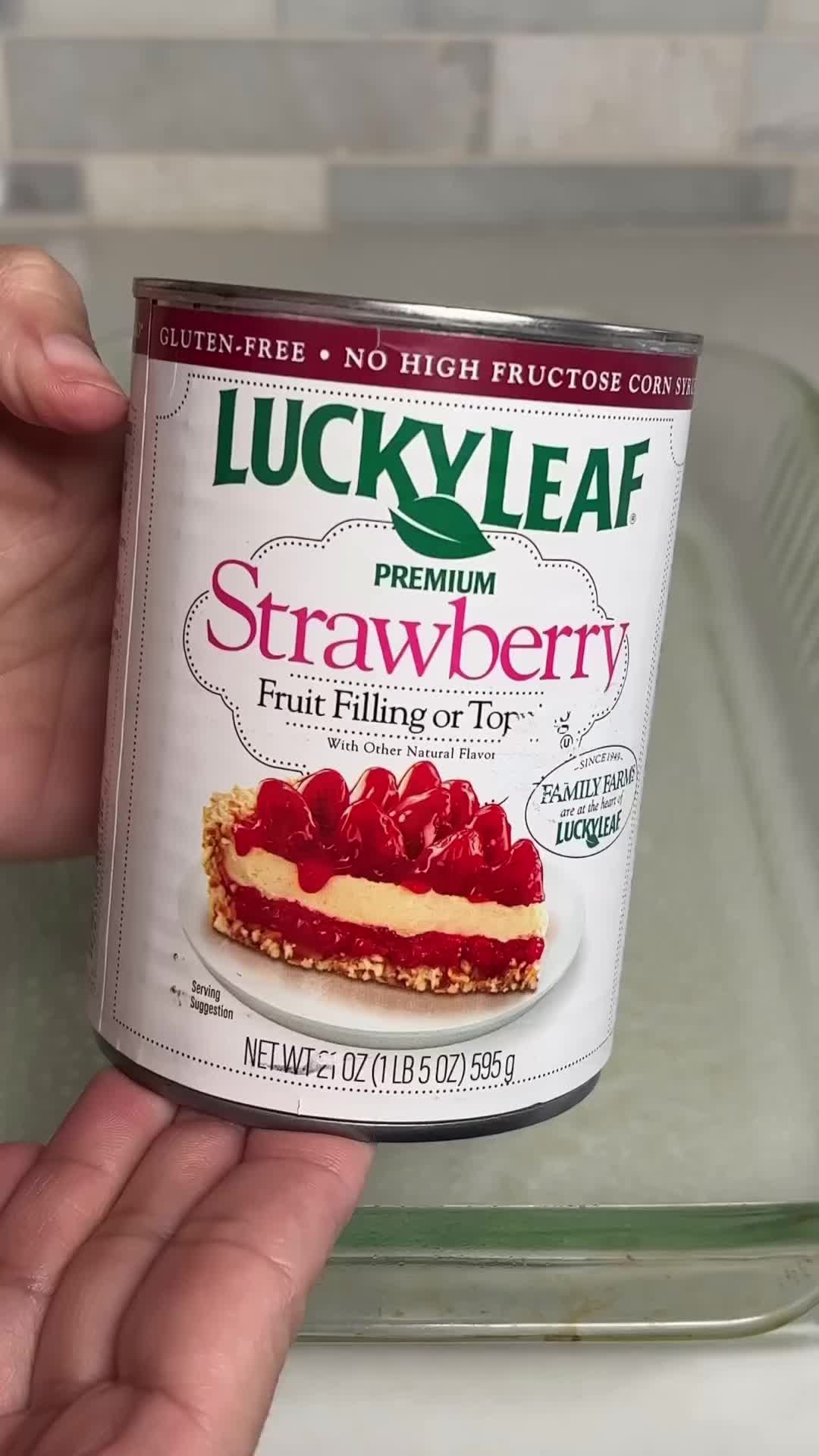 This may contain: a woman holding a bowl of strawberry cheesecake with a spoon in her hand and the words four ingredient strawberry cheesecake dump cake