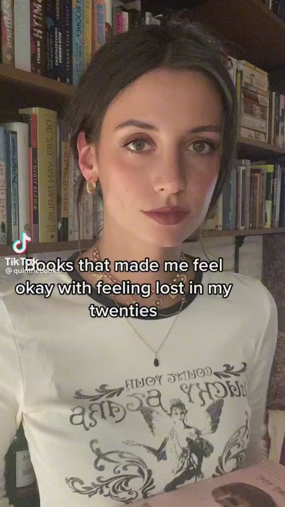 This may contain: a woman holding a book in front of a bookshelf with a quote on it