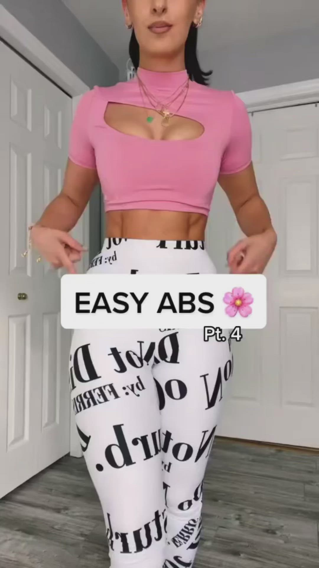 This may contain: a woman in pink shirt and white pants holding up a sign that says easy abs