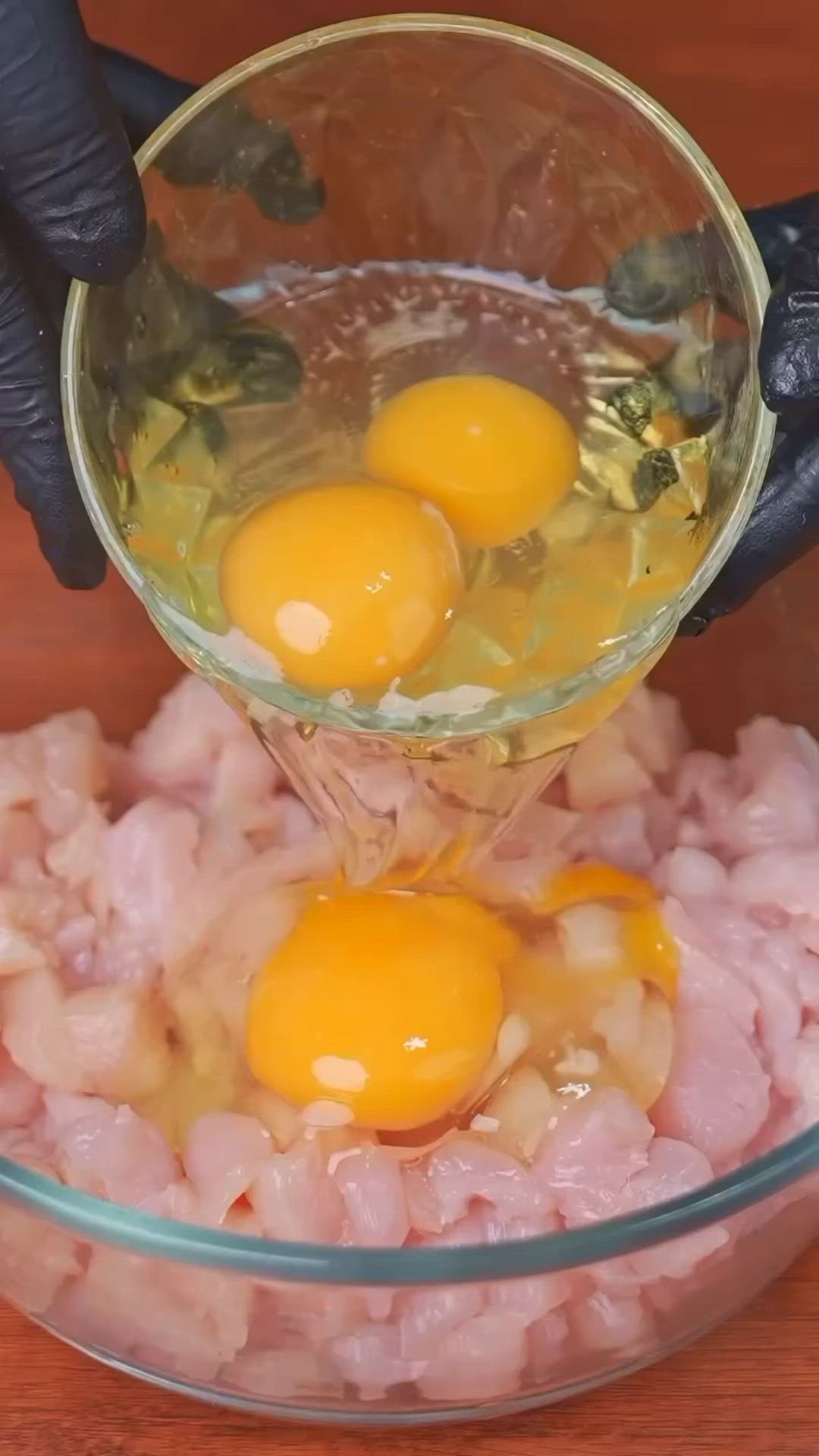 This may contain: two eggs are being added to the meat in a glass bowl on a wooden table