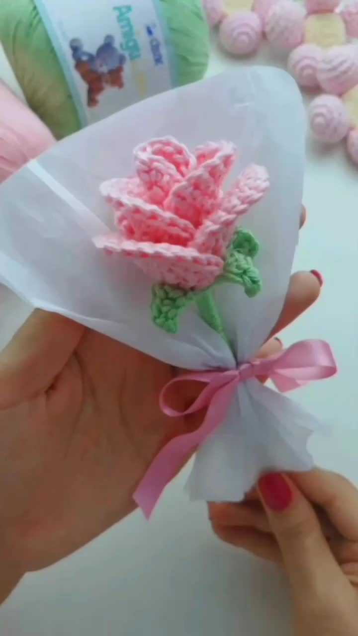 This may contain: a person is holding some paper with flowers on it and pink ribbon around the end