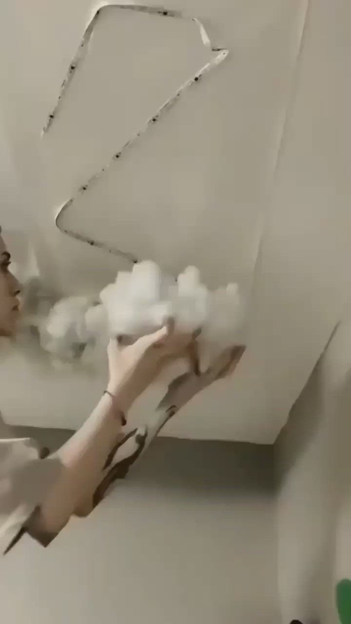 This may contain: a woman is holding cotton in her hand and she is painting the ceiling with white paint