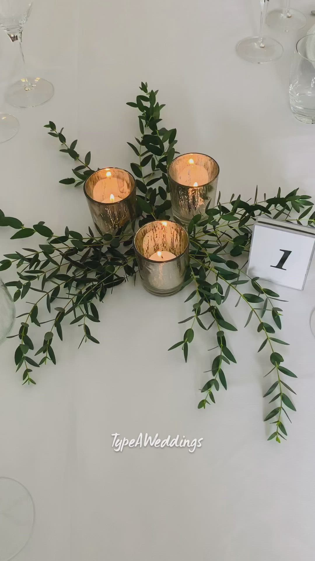 This may contain: three candles are sitting on top of a table with greenery and place cards in front of them