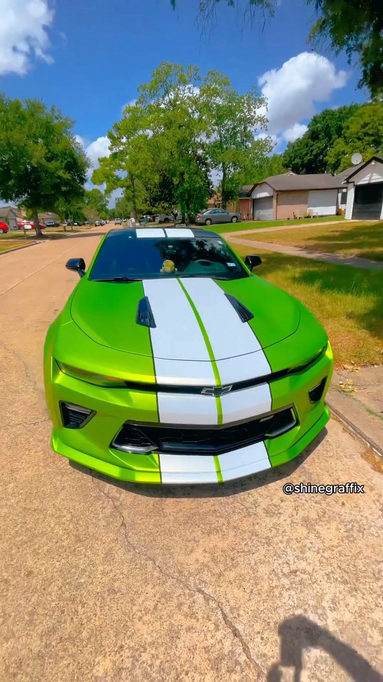 This may contain: the green and white car is parked on the side of the road in front of some houses